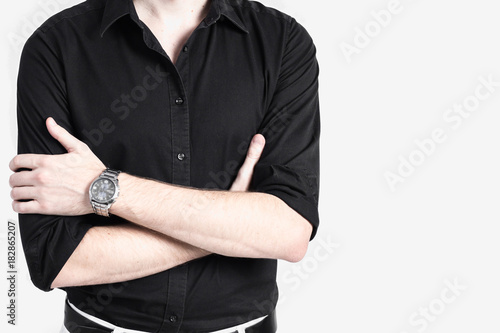 Handsome young man in a black shirt leaning against a light gray wall and looking at the camera
