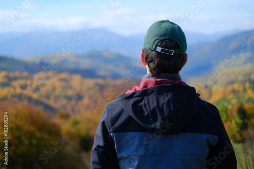 A single man in grey coat standing on mountain hill and watching and njoying a valley view, blurred backgroud, view from back © stebliuk