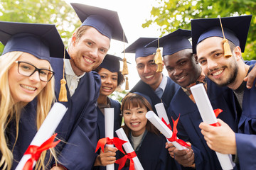 happy students in mortar boards with diplomas