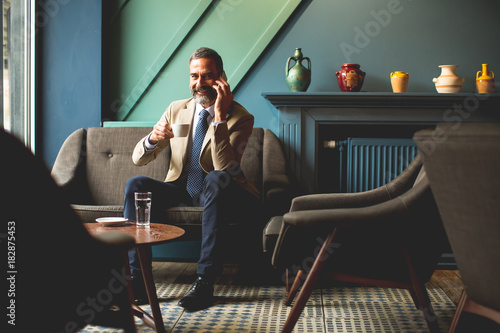 Middle-aged businessman drinking coffee and uses mobile phone in the loby photo