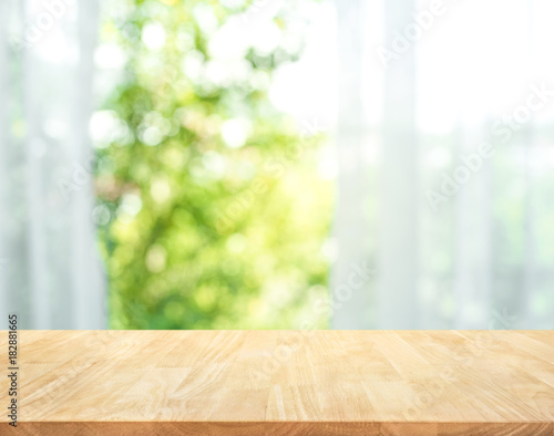 Empty of wood table top on blur of curtain with window view green from tree garden background.