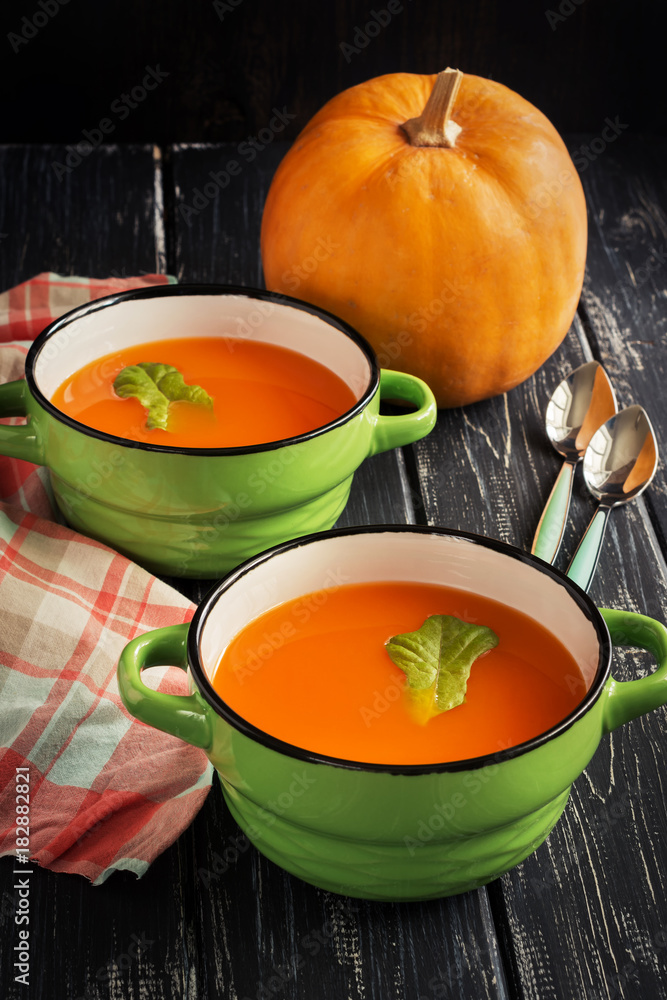 Pumpkin soup puree in ceramic small green saucepans on a wooden table. Pumpkin soup puree in ceramic small green saucepans on a wooden table.