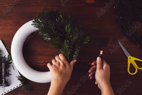 Female florist fixing branches on christmas wreath, top view