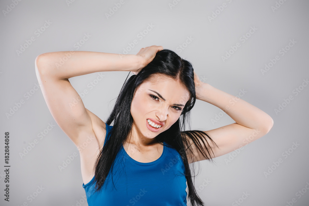 young woman with long brunette hair in blue dress giving angry emotion in photostudio on gray background