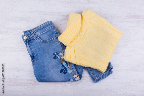 Blue jeans and yellow sweater on white wooden background. Women's fashion clothes.