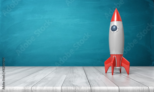 Fototapeta Naklejka Na Ścianę i Meble -  3d rendering of a red and silver realistic model of a retro rocket stands on a wooden desk on a blue background.