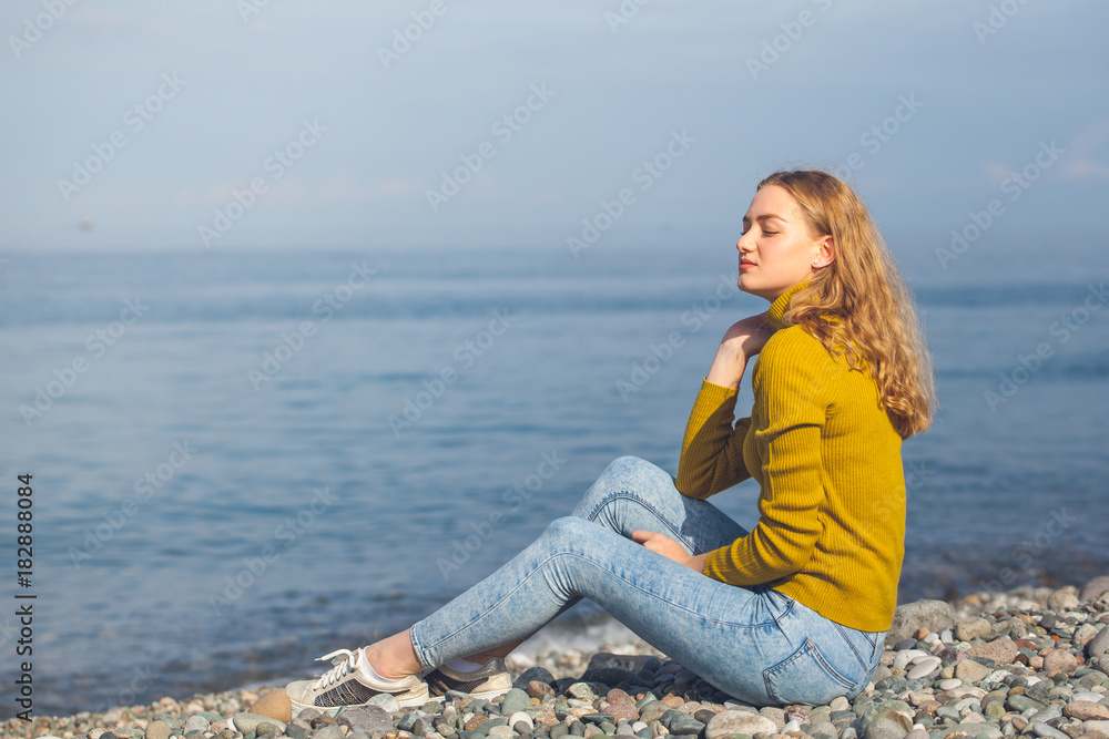 beautiful blonde girl is sitting on the beach and looking at the horizon