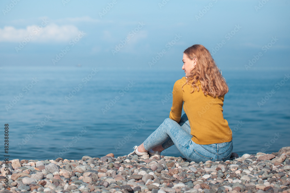 beautiful blonde girl is sitting on the beach and looking at the horizon beautiful blonde girl is sitting on the beach and looking at the horizon