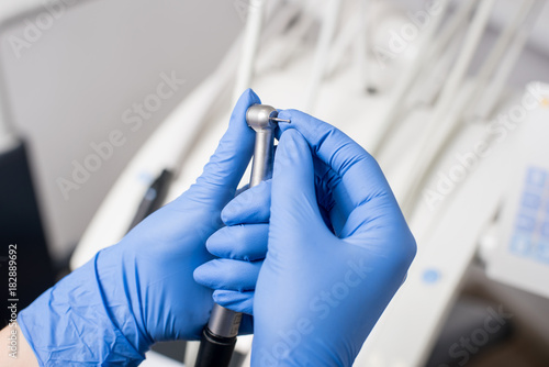 Dentist's hands with blue gloves fixing dental drill in dental office. Close up, selective focus. Dentistry