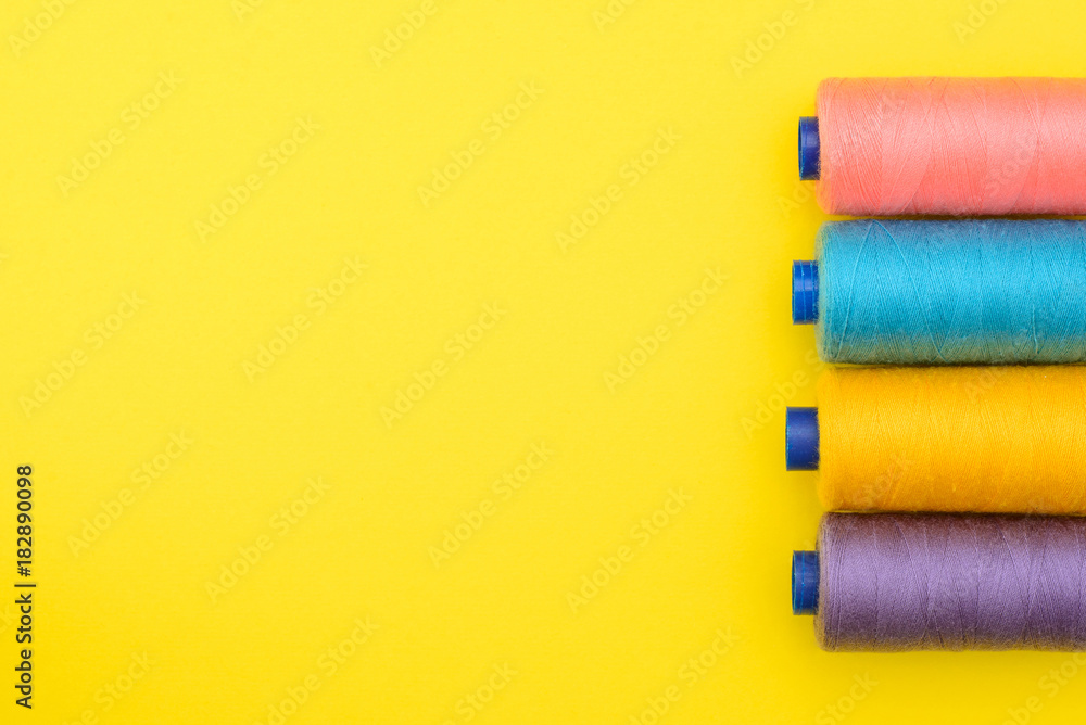 multicolored thread coils on yellow background with a blank space under an inscription in the middle. The concept of sewing production. Top view, Flat Lay. multicolored thread coils on yellow background with a blank space under an inscription in the middle. The concept of sewing production. Top view, Flat Lay.