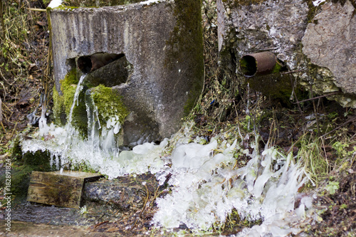 Mineral water spring tap in forest. Old stone ecological clean drinking water tap coming out from a stone wall covered with green moss. photo