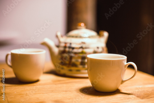 Teapot and 2  white cups with hot tea on  wooden table. Tea drinking time. Vintage image effect.  Natural mood.