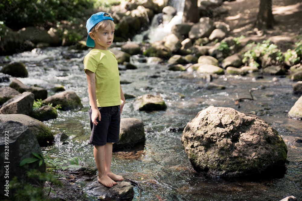 5 year old boy with a funny face standing on a rock in a stream 5 year old boy with a funny face standing on a rock in a stream
