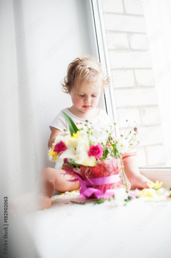 The baby sits on the windowsill and considers a bouquet of flowers The baby sits on the windowsill and considers a bouquet of flowers