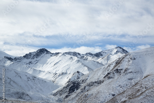 Зимний пейзаж. Красивые горы в снегу, белые облака на синем небе над живописным ущельем. Припрда Северного Кавказа