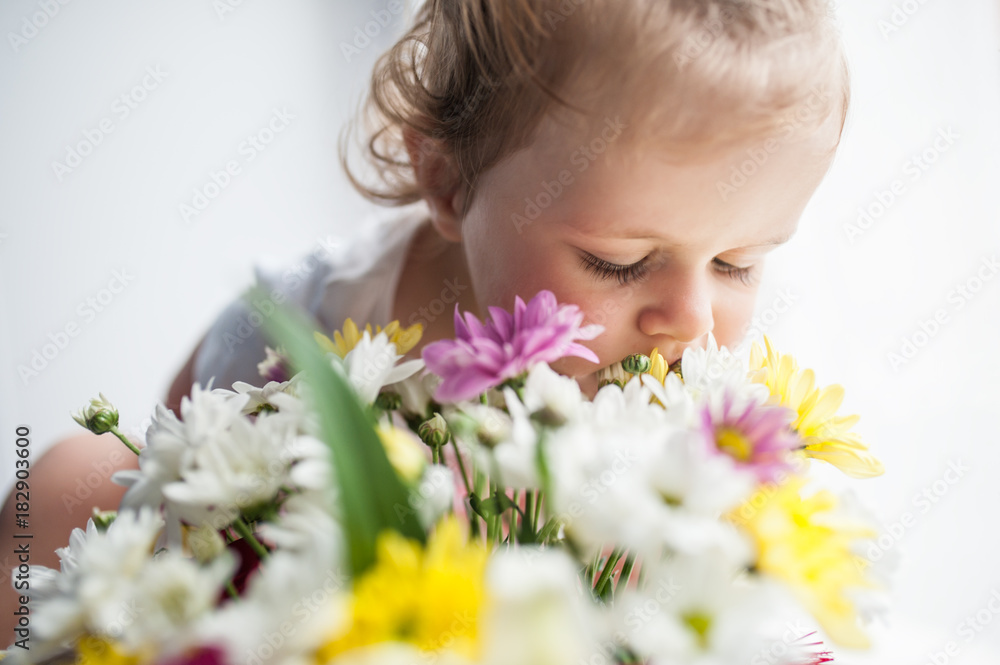 Baby sitting and sniffing a bouquet of flowers from small chrysanthemums, closing his eyes and sticking his nose in the flowers Baby sitting and sniffing a bouquet of flowers from small chrysanthemums, closing his eyes and sticking his nose in the flowers