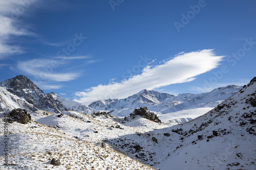 Зимний пейзаж. Красивые горы в снегу, белые облака на синем небе над живописным ущельем. Припрда Северного Кавказа