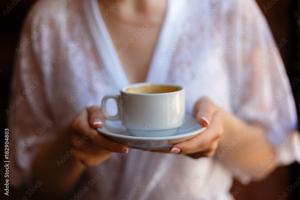 Young girl in Bathrobe with a pattern, drinking coffee on the hotel balcony, enjoying the view and the awakening. Morning girl drinking espresso. Close-up view. Young girl in Bathrobe with a pattern, drinking coffee on the hotel balcony, enjoying the view and the awakening. Morning girl drinking espresso. Close-up view.