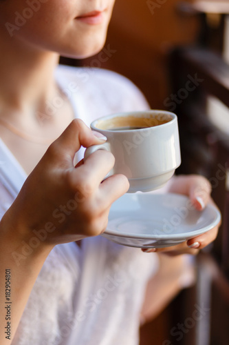 Young girl in Bathrobe with a pattern, drinking coffee on the hotel balcony, enjoying the view and the awakening. Morning girl drinking espresso. Close-up view.