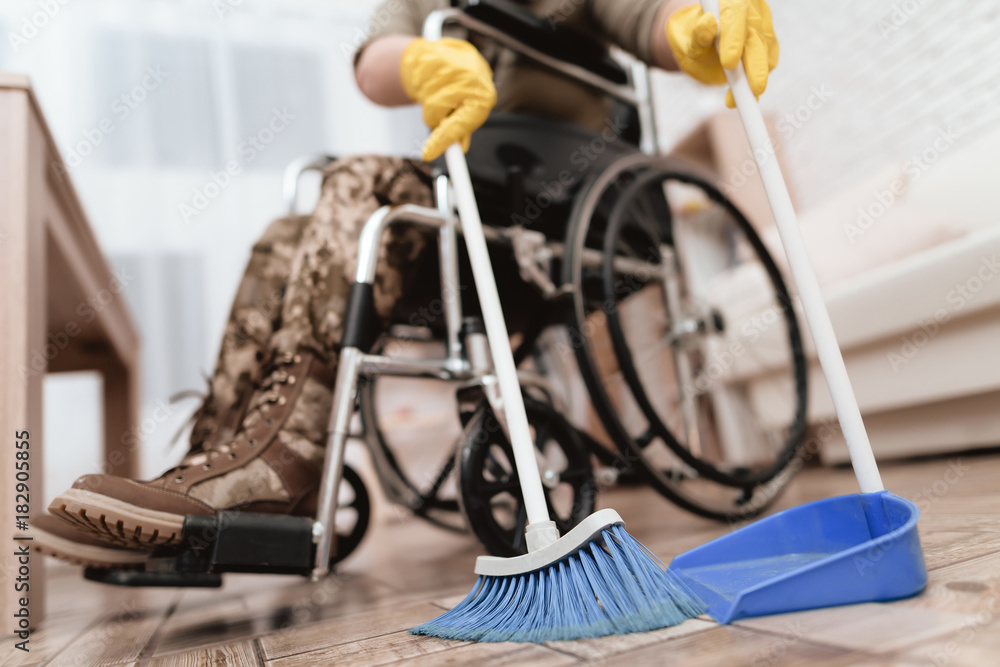Fototapeta premium A female veteran in a wheelchair is cleaning the house. She's in military uniform.