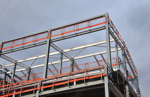 steel frame building under construction with orange safety railings and girders