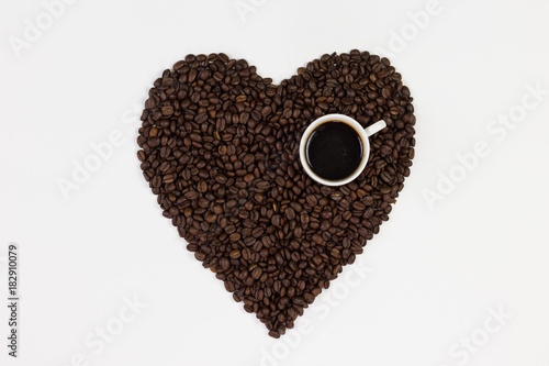 Coffee cup and coffee beans in a form of a heart isolated on white background.