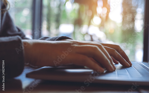 Closeup image of a business woman's hands working and typing on laptop keyboard on wooden table