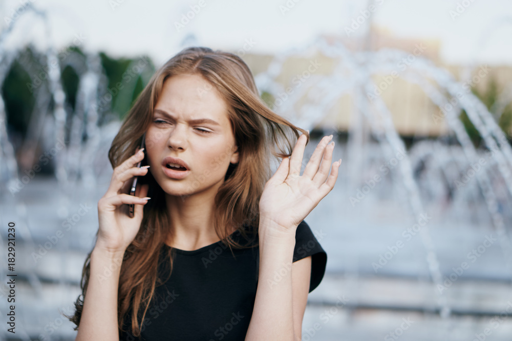Young beautiful woman calls on the phone in the street in the city near the fountain