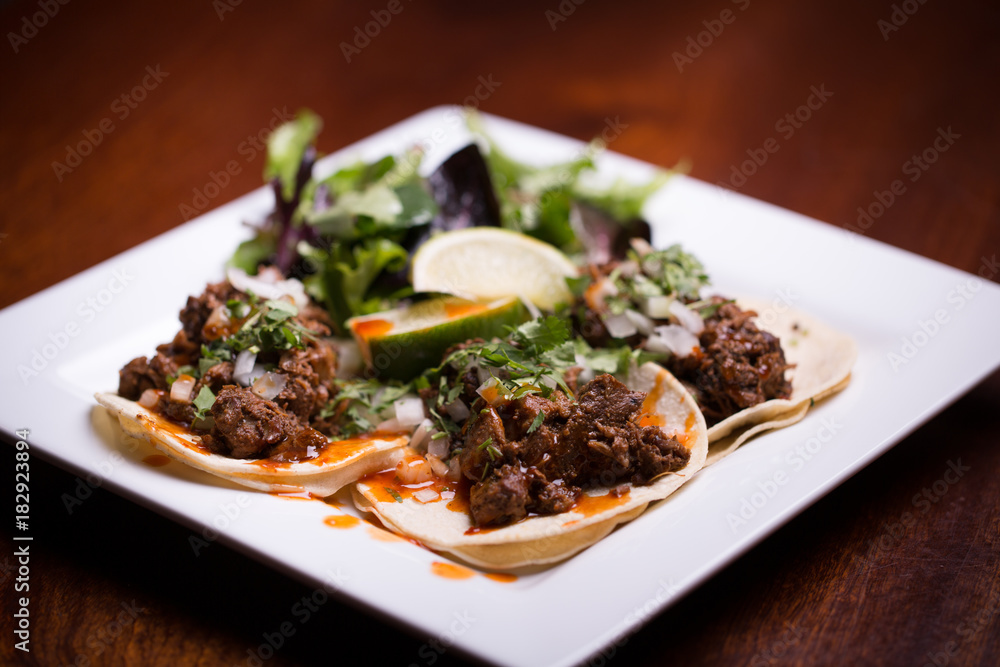 Gourmet beef tacos on square plate under dramatic light