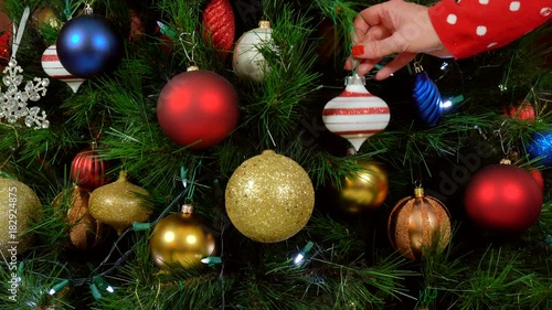 Festive Christmas Tree with brightl color decorations, woman hanging last ornament. photo