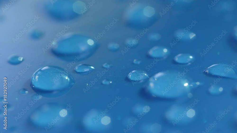 DOF, MACRO, CLOSE UP: Big and small shiny water drops on the surface of a wet light blue car's roof. Reflecting waterdrops on blue surface. Shiny liquid bubbles on wet car roof after light showers. DOF, MACRO, CLOSE UP: Big and small shiny water drops on the surface of a wet light blue car's roof. Reflecting waterdrops on blue surface. Shiny liquid bubbles on wet car roof after light showers.