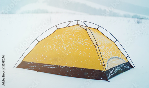 a yellow tent covered with snow on a cold winter day. Winter tent camp in the snow forest
