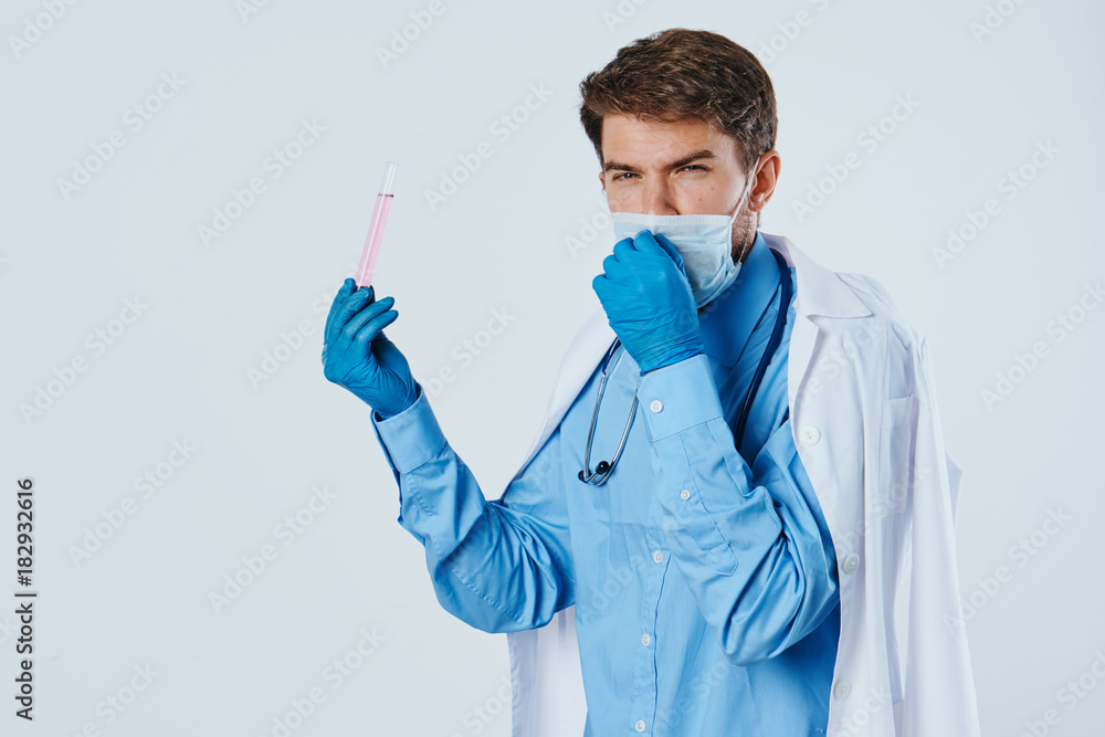 Man with a beard on a light background in a medical mask holds laboratory utensils, doctor, medicine, science Man with a beard on a light background in a medical mask holds laboratory utensils, doctor, medicine, science