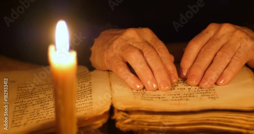 Elderly woman reading old book by candlelight

