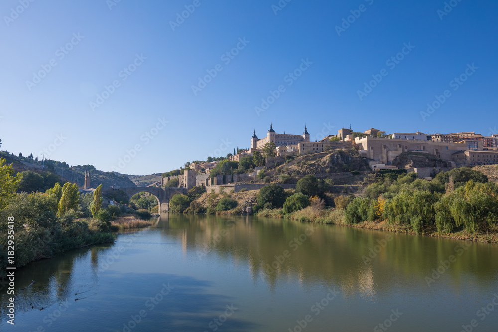Scenery of Toledo city, in Spain, Europe. Green water river Tagus, Alcantara arch bridge, landmark and monument from ancient Roman age, and alcazar building

