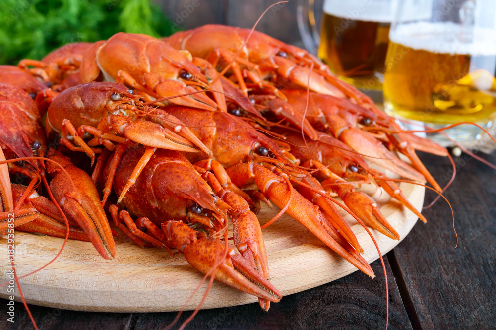 A pile of large crawfish on a wooden tray, glasses with beer on a dark wooden background. A pile of large crawfish on a wooden tray, glasses with beer on a dark wooden background.