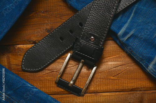 leather belt with buckle and jeans on wooden background, top view