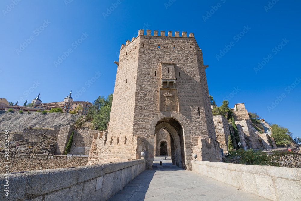 tower with door of Alcantara bridge, landmark and monument from ancient Roman and arab age, with Alcazar and Toledo city in background, Spain, Europe
