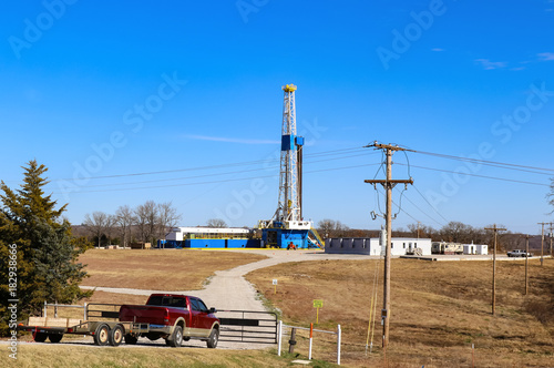 Drilling Rig and site for large oil-gas well with buildings and equipment - red truck with trailer at closed gate leading down to it