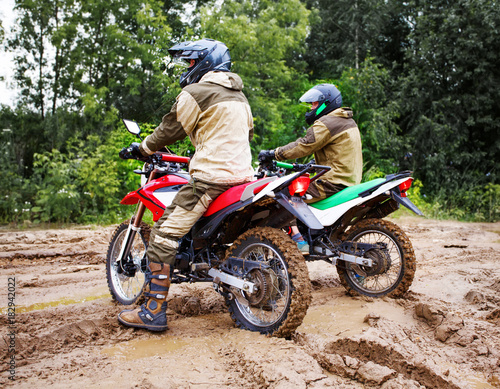 Two mens on a motorcycle rides through the mud
