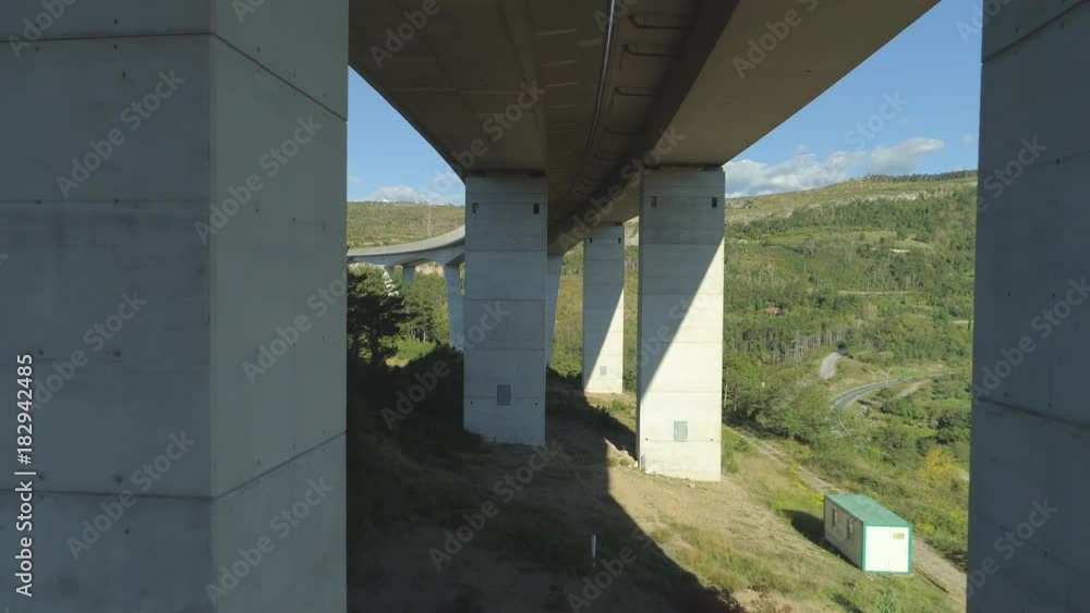 AERIAL: Massive concrete viaduct providing an alternative route for traffic to navigate through urbanized landscape. Flying between pillars of a large overpass junction surrounded by pine forests. AERIAL: Massive concrete viaduct providing an alternative route for traffic to navigate through urbanized landscape. Flying between pillars of a large overpass junction surrounded by pine forests.
