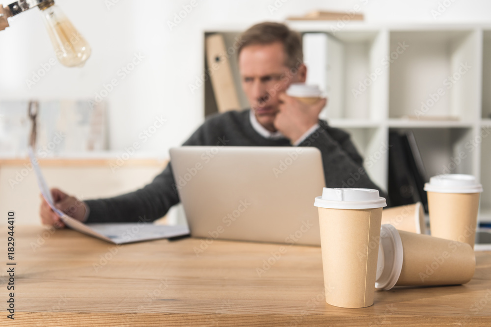 tired middle aged businessman working with laptop and drinking a lot of coffee tired middle aged businessman working with laptop and drinking a lot of coffee