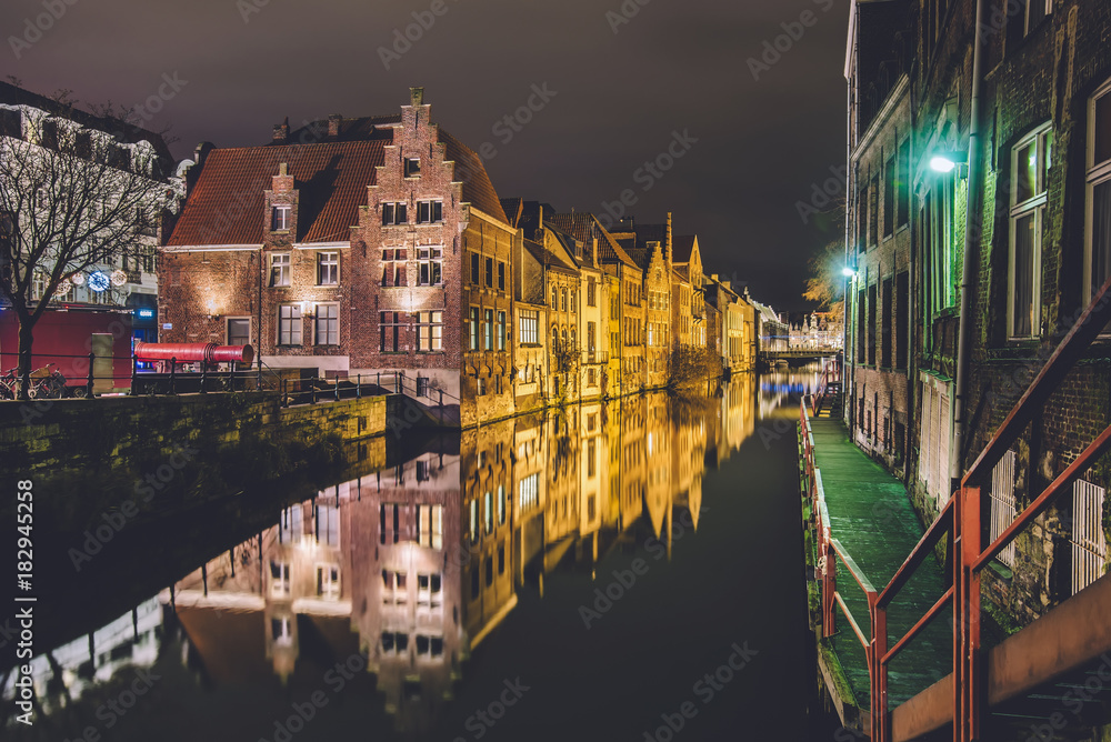 Ghent, Flanders, Belgium - January 3th, 2017. Red cannon Dulle Griet and medieval brick merchant houses reflected in night canal by evening illumination in historical Gent city center.