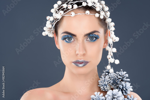 portrait of beautiful woman with hair accessory, christmas pine cones, winter makeup and glitter, isolated on grey