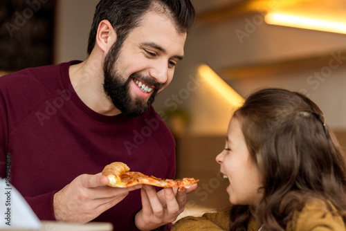 father giving daughter to bite a piece of pizza
