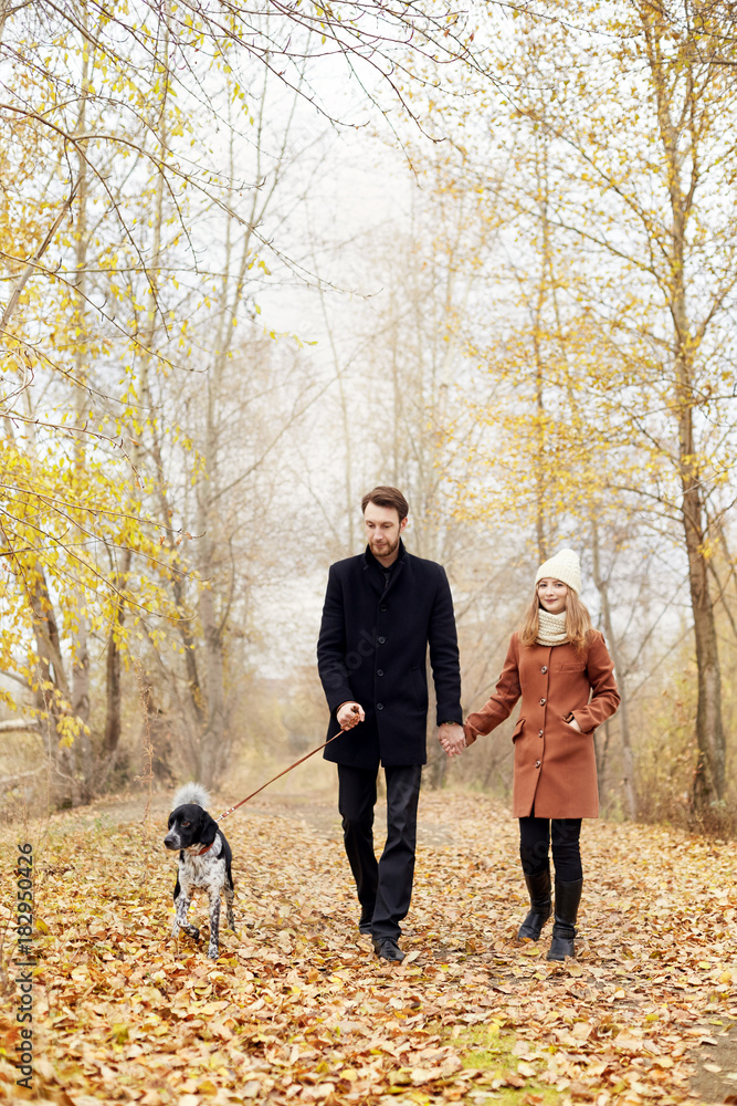 Fototapeta premium Couple walking with dog in the Park and hugging. Autumn walk men and women with a dog. Romance and love on an autumn landscape