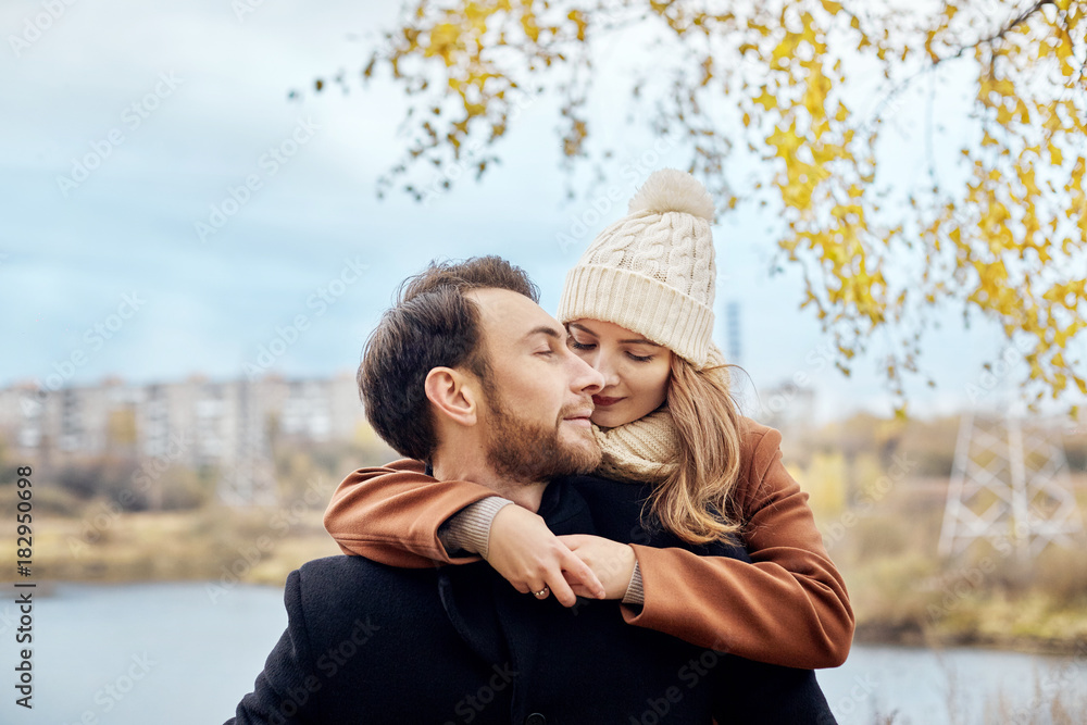 Fototapeta premium Loving couple walking in Park in autumn hugs and kisses. Autumn walk men and women in the woods on the fallen leaves. Romance and love on an autumn landscape
