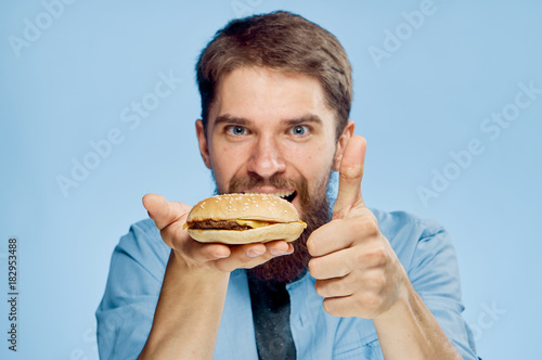 Man with a beard on a blue background holds a hamburger, fast food, portrait, emotions