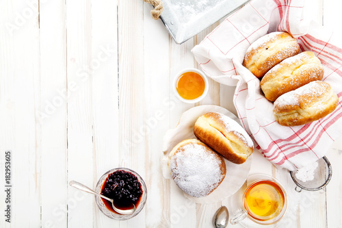 Tea time with festive sufganiyot donuts filled with jelly and covered with sugar powder. White wooden background, bright lighting. Horizontal composition.