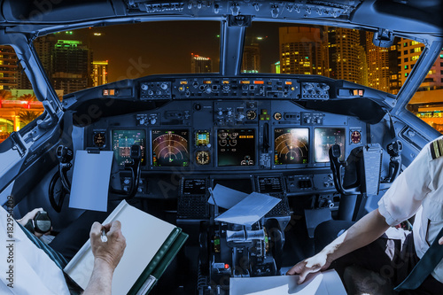 Airplane cockpit flying on Dubai Marina by night, United Arab Emirates, with pilots arms and blank white papers for copy space.